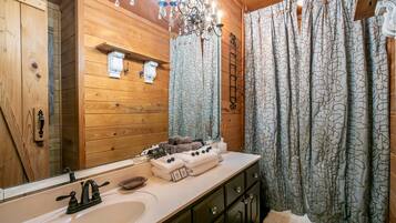 Ein Badezimmer im Holzblockhaus-Stil mit einem großen Spiegel, Holzschränken, einem Waschbecken und einer Pendelleuchte.