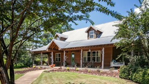 A wooden cabin with a metal roof, a covered porch, and a well-maintained lawn. - The CPL, 3BR Oxford Retreat by Velvet Ditch Villas (Batesville)