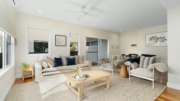 A spacious living room with a beige sofa, a wooden coffee table, and a ceiling fan. - Coastal Trio-Coral Villa 1 (Huskisson)