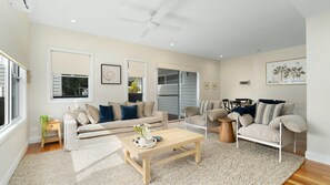 A spacious living room with a beige sofa, a wooden coffee table, and a ceiling fan. - Coastal Duo-Coral Villa 1 (Huskisson)