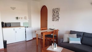 En kompakt opholdsstue med spiseplads, sofa og tekøkken.