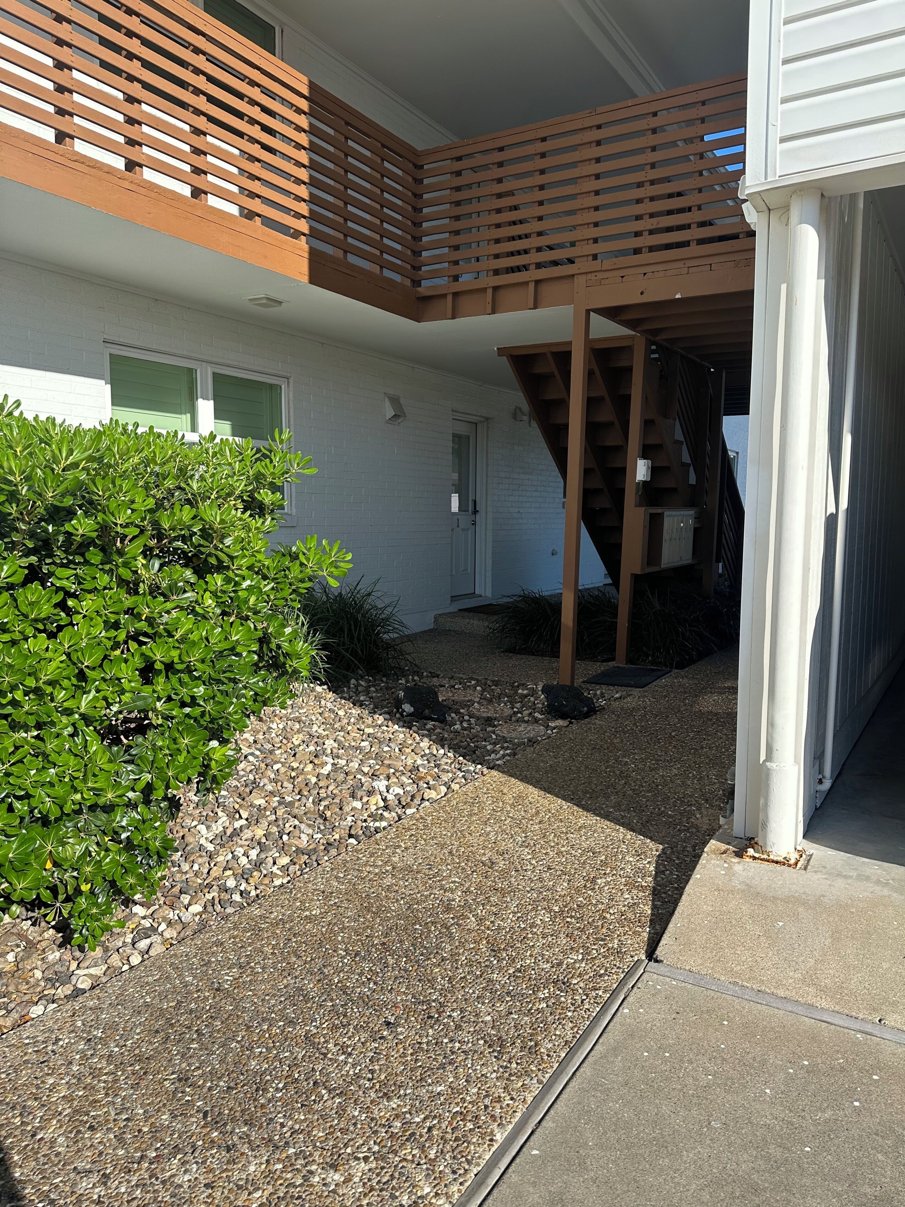 Un edificio residencial con un patio cubierto, una escalera y un camino de grava.