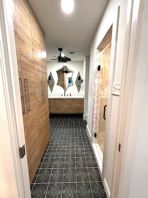 A narrow hallway with a wooden wardrobe, a ceiling fan, and a tiled floor.