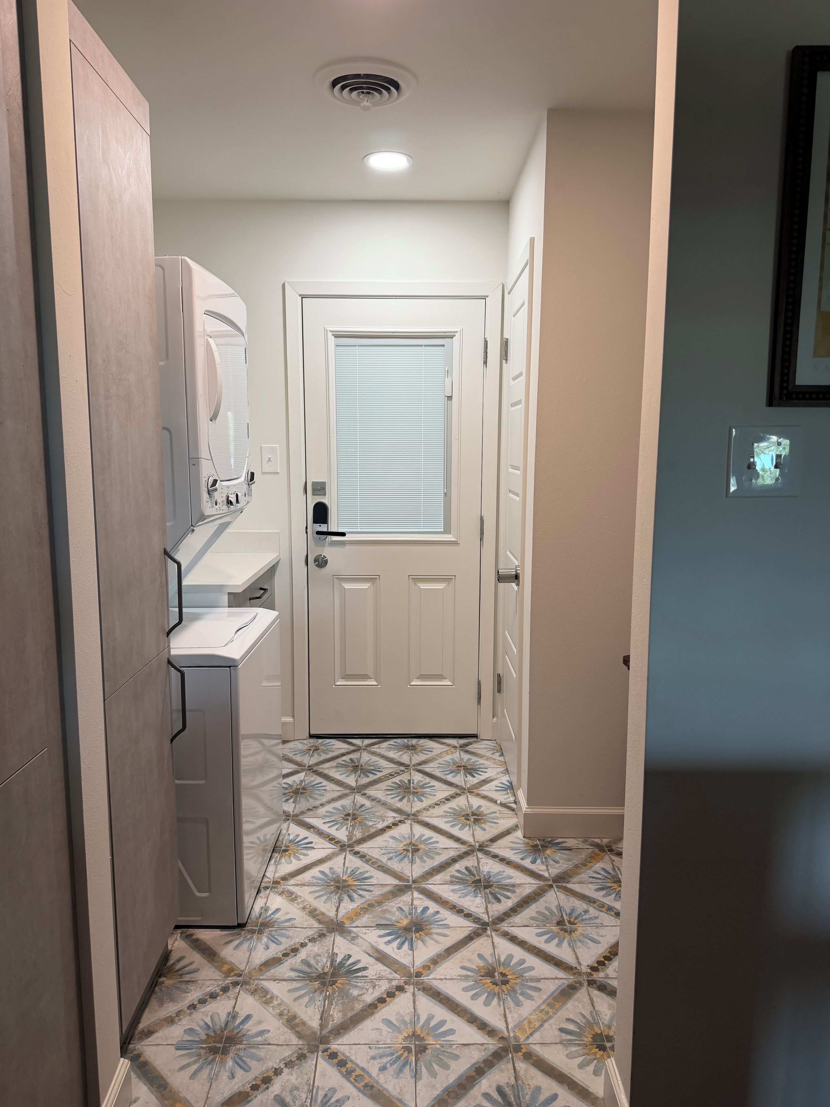 A narrow hallway with a washing machine, a door with a window, and patterned floor tiles.