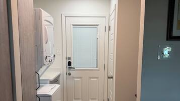 A narrow hallway with a washing machine, a door with a window, and patterned floor tiles.