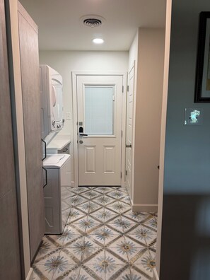 Un couloir étroit avec un lave-linge, une porte dotée d’une fenêtre et des carreaux de sol à motifs.