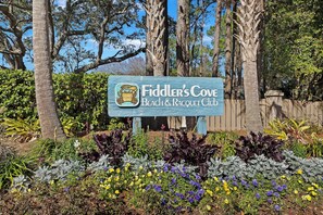 A sign for Fiddler's Cove Beach & Racquet Club surrounded by lush greenery and trees. - Charming two  Bedroom includes: Pool's,  Hot Tub, Fitness Center Walk to Beach ! (Hilton Head Island)