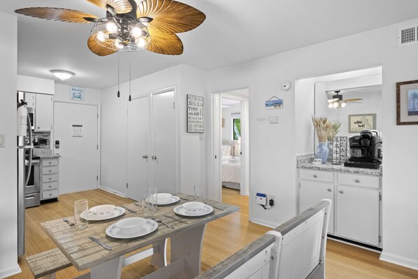A modern kitchen with white cabinets, a dining table set with plates and glasses, and a ceiling fan with lights.