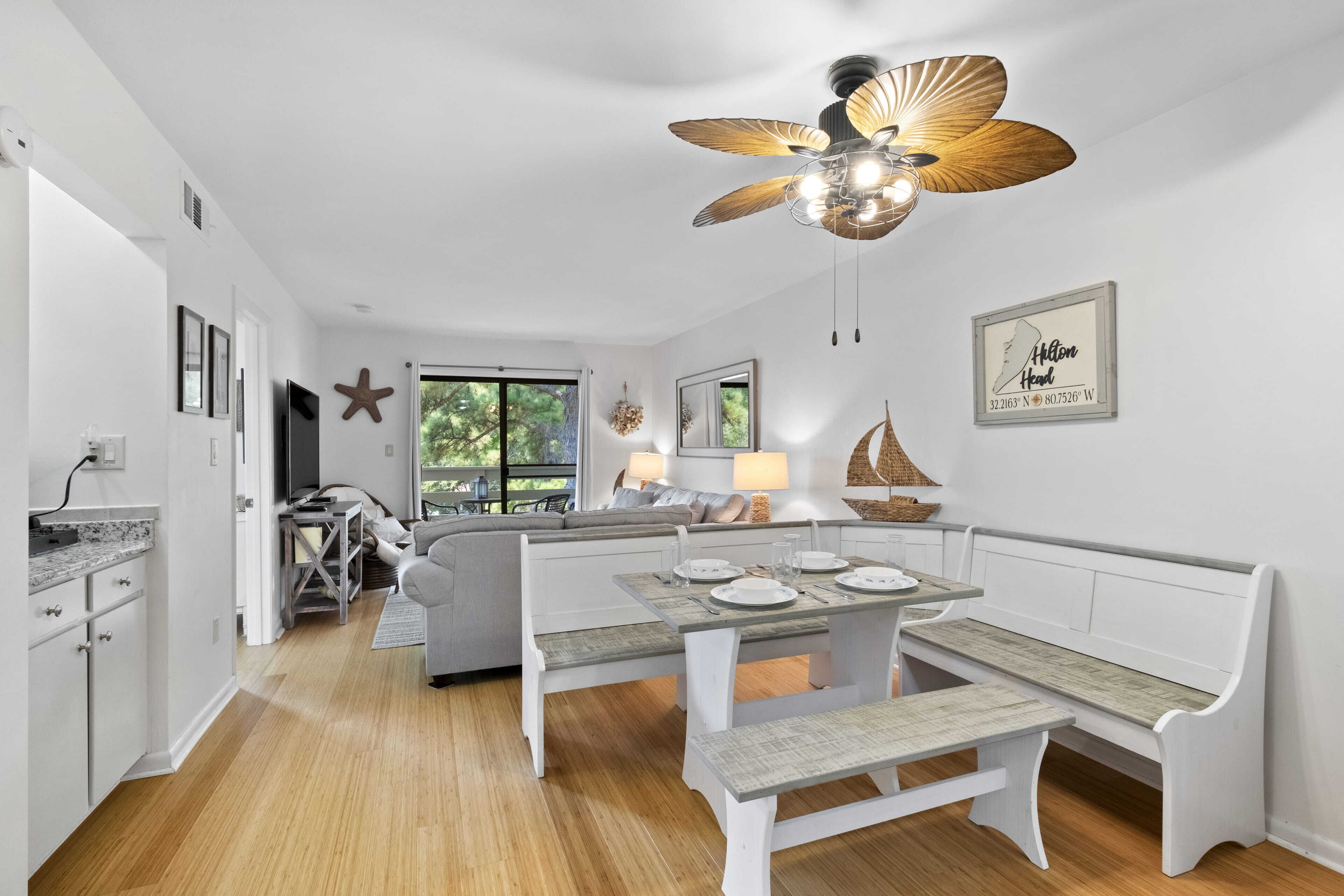 Une cuisine moderne avec des meubles blancs, un coin repas doté d’un banc en bois et un ventilateur de plafond.