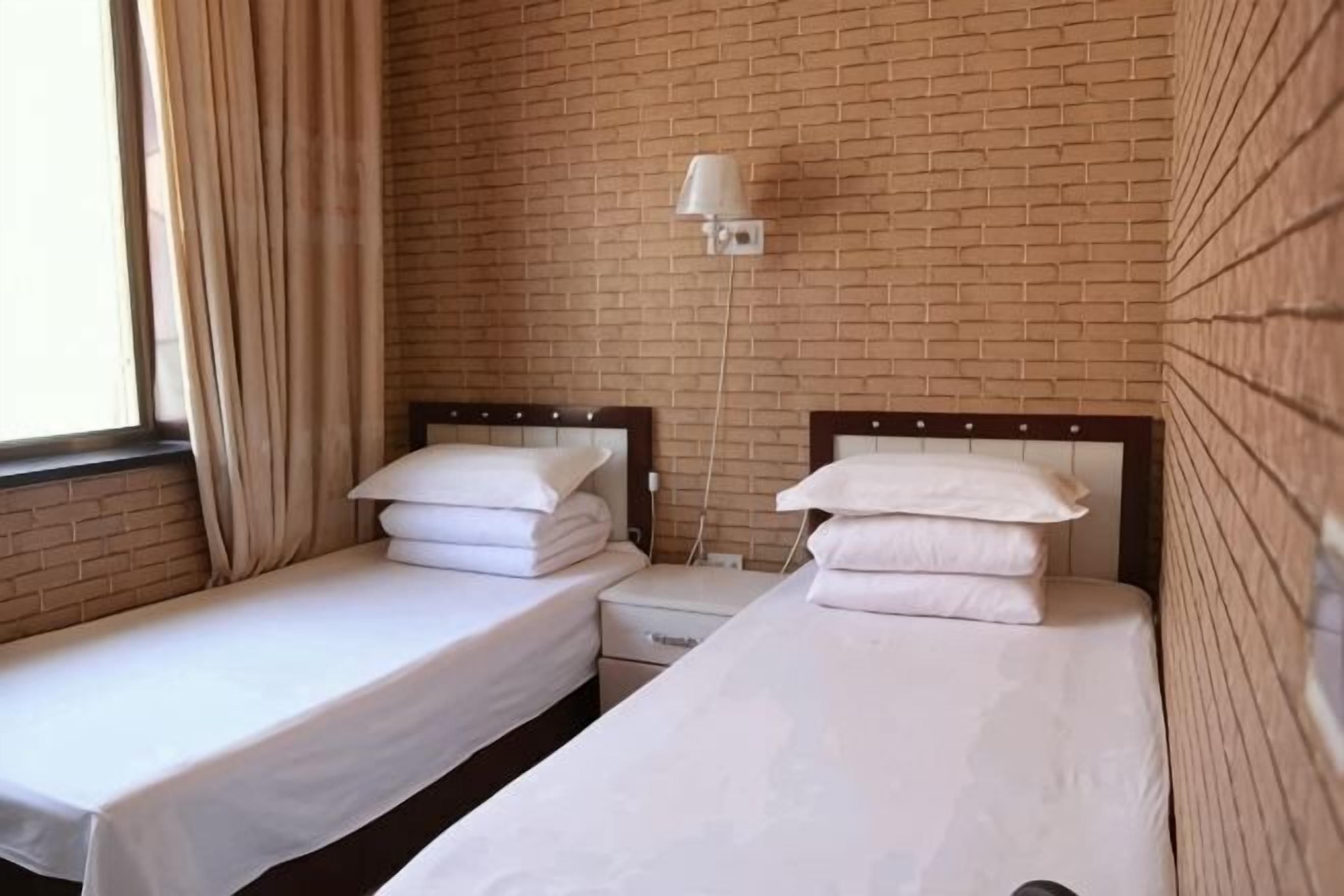 Ein Hotelzimmer mit zwei Einzelbetten, einem Nachttisch, einer Lampe und einer Ziegelwand.