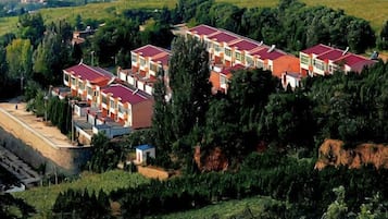 A cluster of buildings with red roofs, surrounded by greenery and hills.