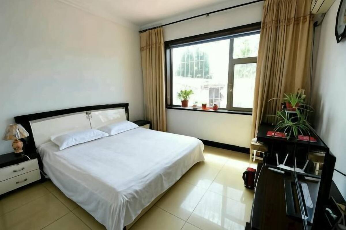 Ein Hotelzimmer mit Bett, Schreibtisch, Stuhl, einem Fenster mit Vorhängen und einer Zimmerpflanze.