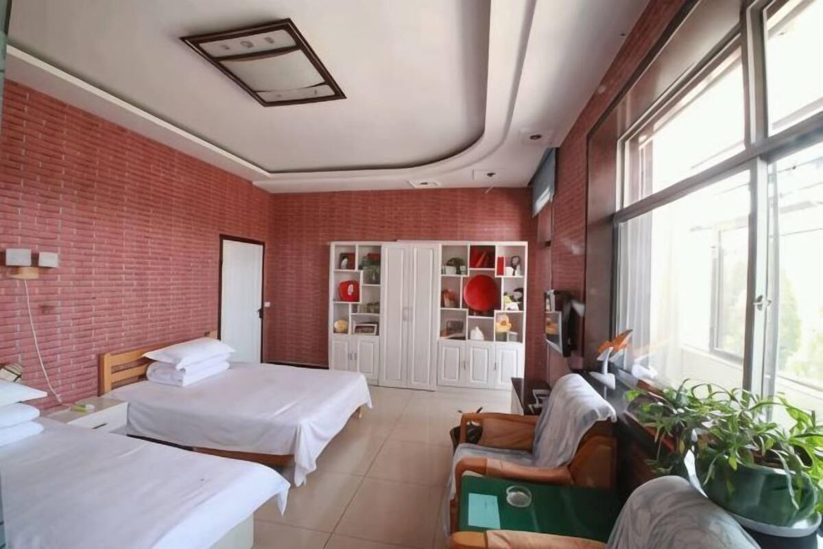 Ein Hotelzimmer mit zwei Betten, einer Couch, einem Fernseher, einer Ziegelwand und einem Fenster.