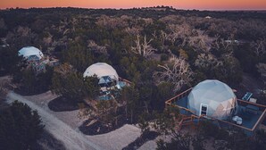 Trois structures en forme de dôme, entourées d’arbres et reliées par des passerelles en bois.