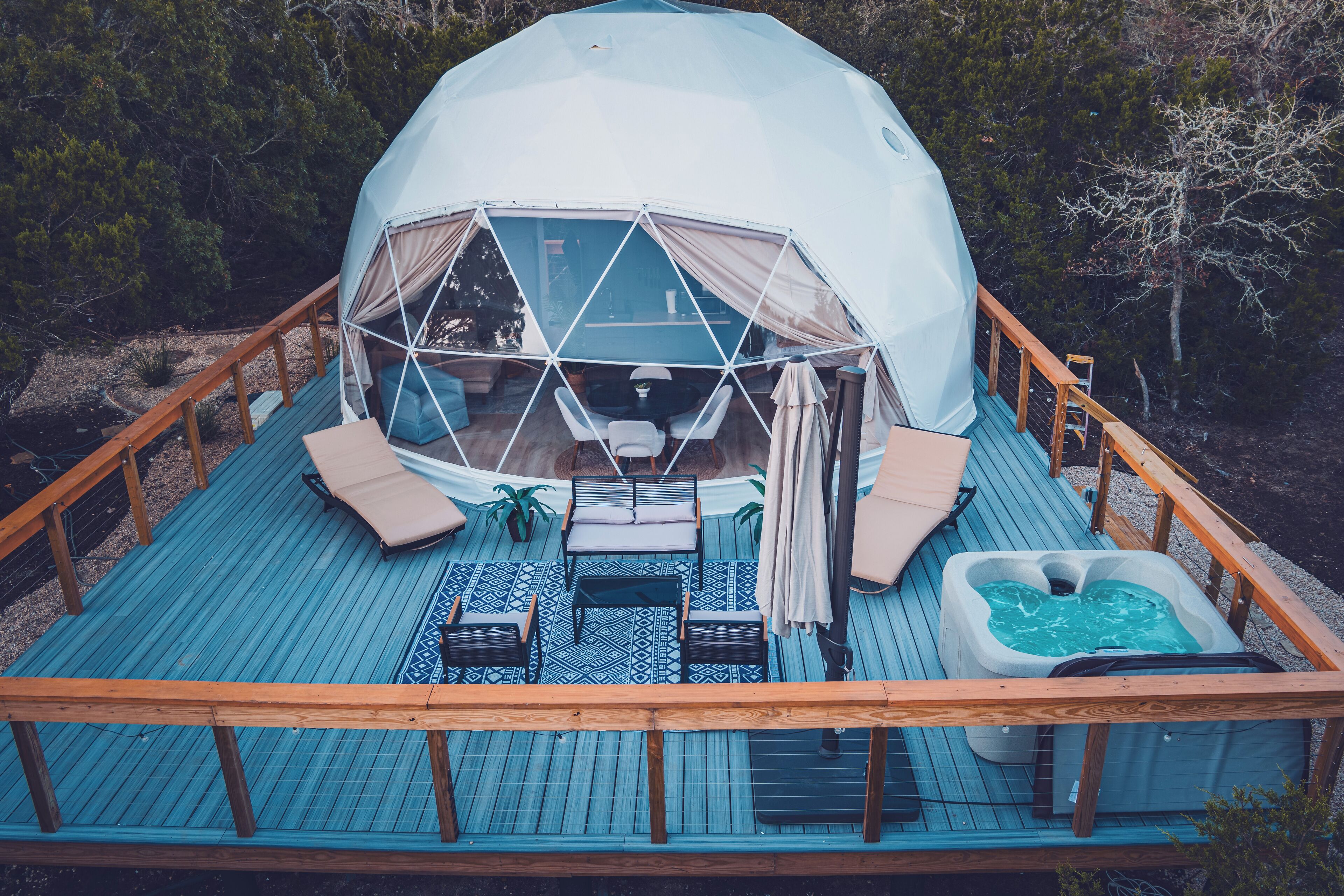 A dome-shaped tent with a wooden deck, lounge chairs, a hot tub, and a small table.