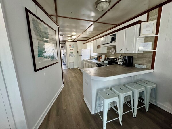A kitchen with white cabinets, a central island with stools, and a framed picture on the wall.