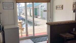 Et lille, hyggeligt rum med trægulv, et lille tekøkken, en bar samt en skydedør til en udendørs terrasse.