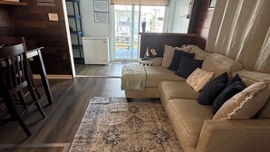En stue med en beige sofa, et tæppe med mønster, trægulv og en loftventilator.
