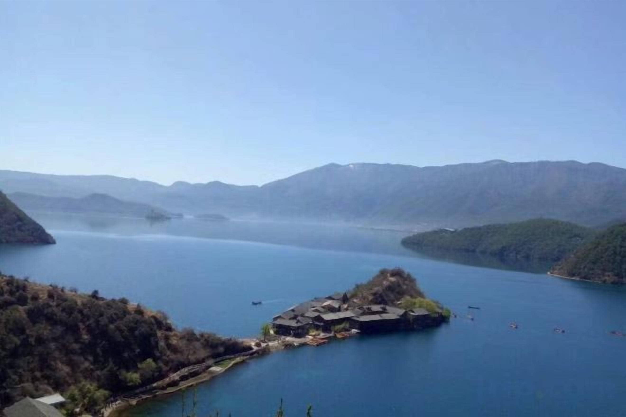 Un lac avec une petite île et des bâtiments, le tout entouré de montagnes.