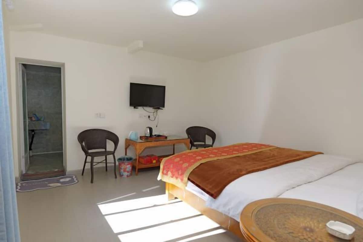 A bedroom with a bed, a desk, a chair, a television, and a small table.