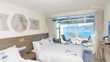 A hotel room with two beds, a desk, and a view of the sea.