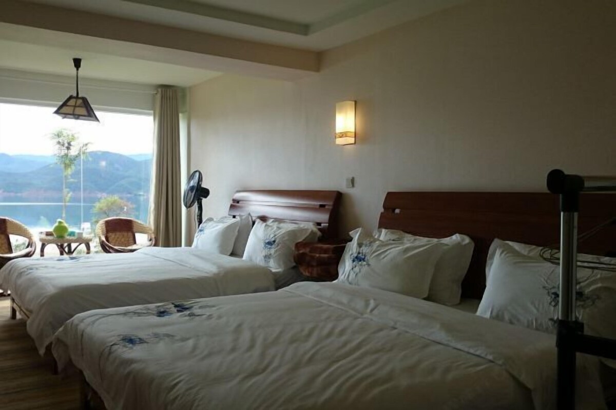 A hotel room with two beds, a sitting area with chairs, a fan, and a view of the mountains.