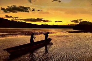 A boat with two people on a calm body of water during sunset.