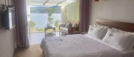 A hotel room with a large bed, a TV, a small table, and a view of a lake.