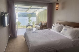 A hotel room with a large bed, a TV, a small table, and a view of a lake.