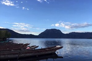 Un lago tranquillo con barche ormeggiate a sinistra, circondato da montagne sotto un cielo sereno.