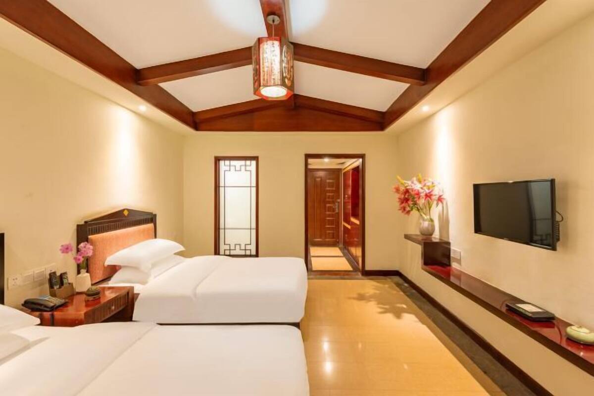 A hotel room with two beds, a TV, a wooden ceiling, and a hallway leading to another room.