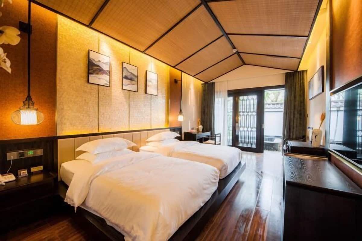 A hotel room with two beds, a wooden floor, a large window, and artwork on the wall.