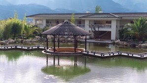 A traditional Japanese-style pavilion over a koi pond, surrounded by a stone bridge and lush greenery, with a mountain backdrop. - Dali Geothermal Paradise Hotel (Eryuan)
