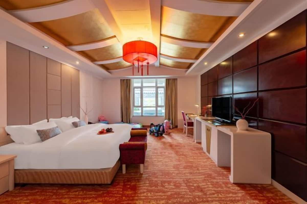 A hotel room with a large bed, a desk, a television, and a red hanging light fixture.
