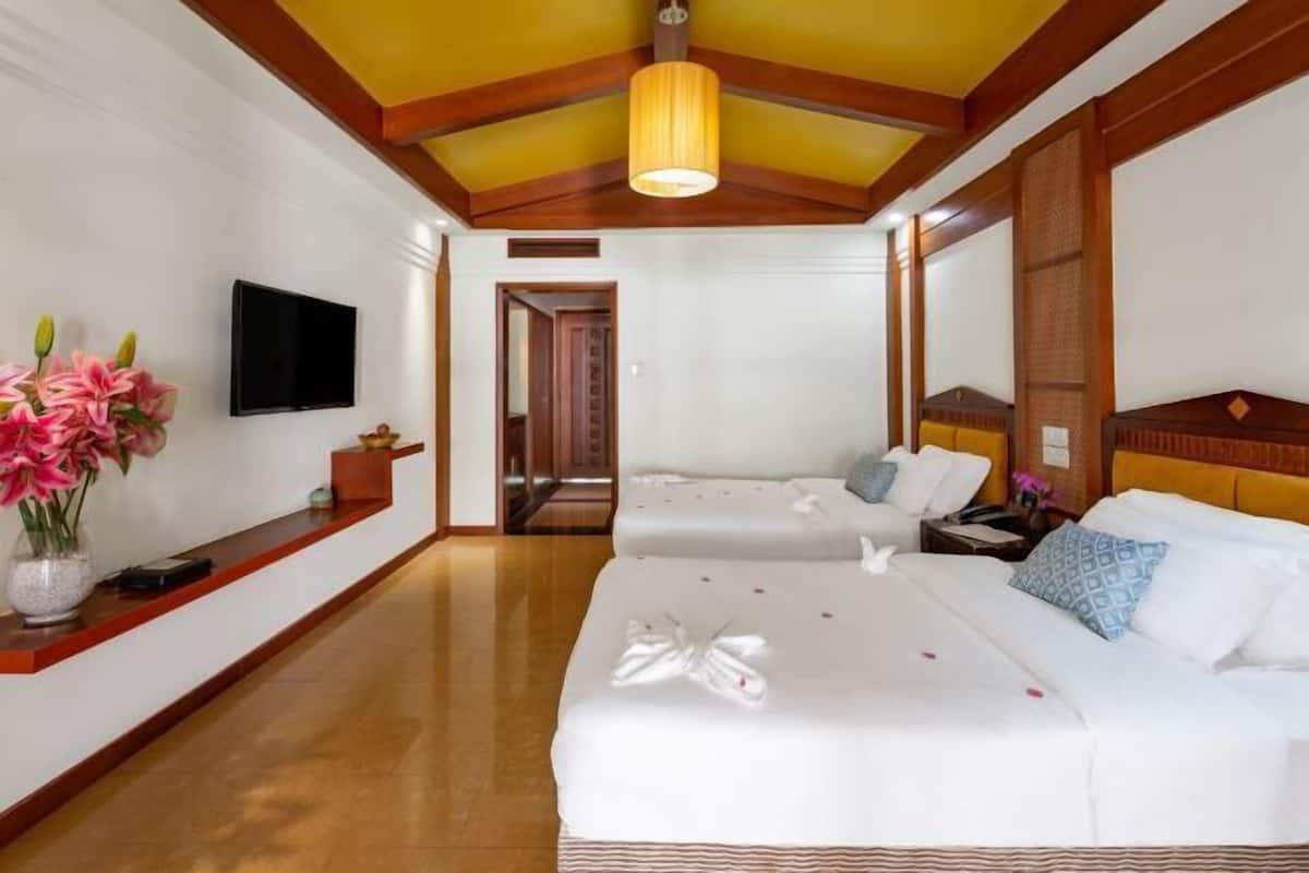 A hotel room with two beds, a TV, a wooden ceiling, and a reception desk with flowers.