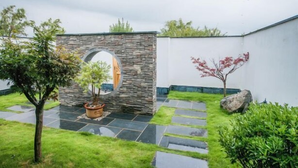 A stone archway leading to a garden area with a potted plant, a large rock, and a small tree. - Dali Geothermal Paradise Hotel (Eryuan)