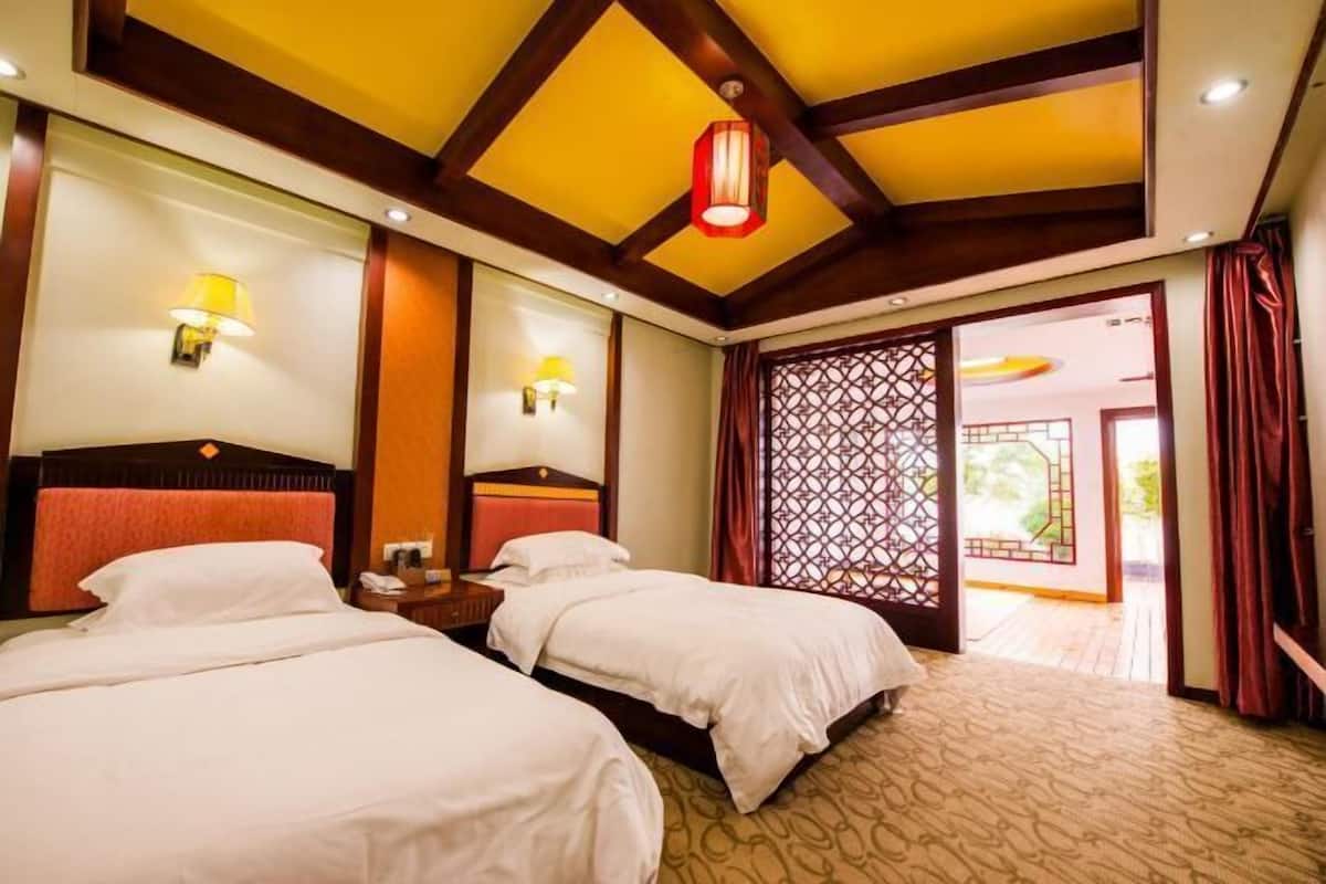 A hotel room with two beds, wooden beams on the ceiling, and a view of the outside through a door.
