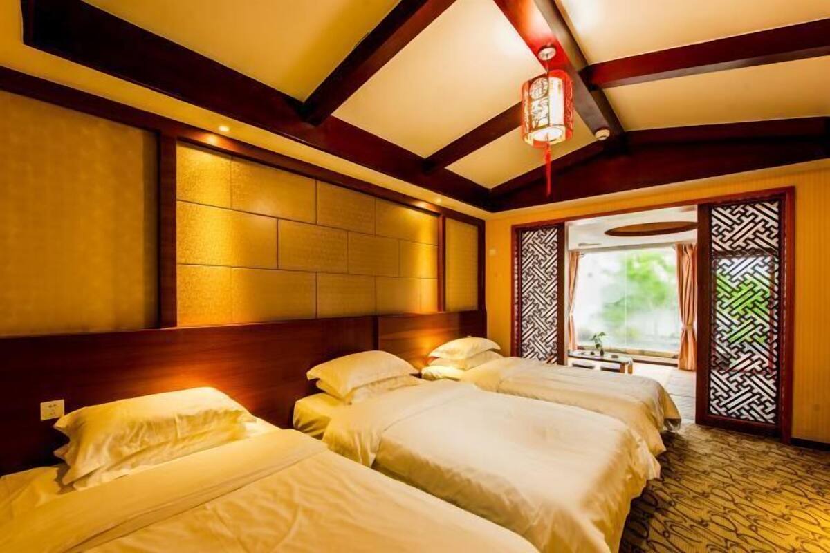 A hotel room with two beds, wooden headboard, and a view of greenery through a patterned door.