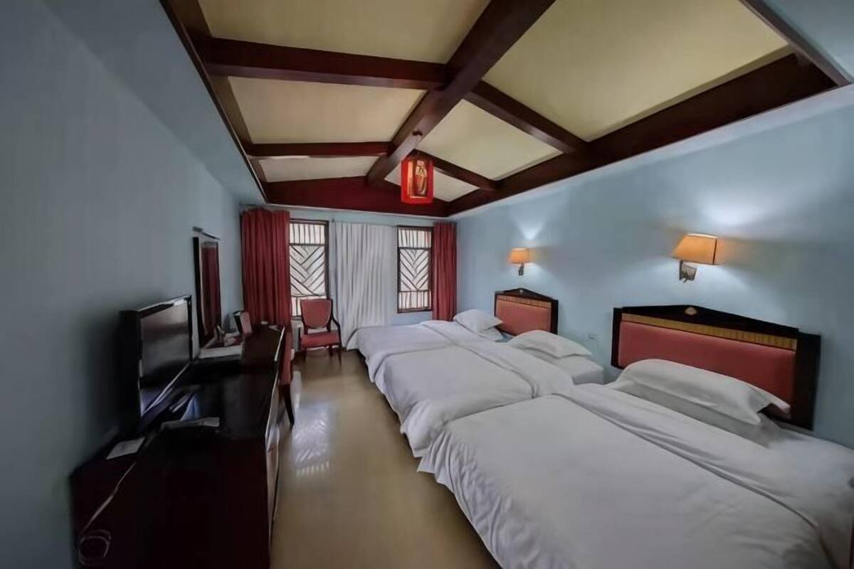 A hotel room with two beds, a TV, a desk, and a window with curtains.
