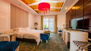 A hotel room with a bed, a desk, a chair, a TV, and a patterned carpet. - Dali Geothermal Paradise Hotel (Eryuan)