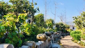 A garden with a water feature, including a stone pathway and metal structures. - Dali Geothermal Paradise Hotel (Eryuan)