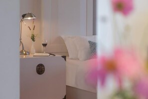 A neatly arranged bedroom with a bedside table, lamp, and a vase with flowers.