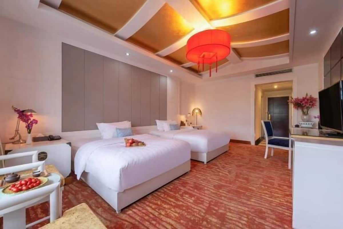 A hotel room with two beds, a desk, a chair, and a television.