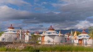 A row of traditional yurts with a stone wall and wooden fence in the foreground. - Dali Geothermal Paradise Hotel (Eryuan)