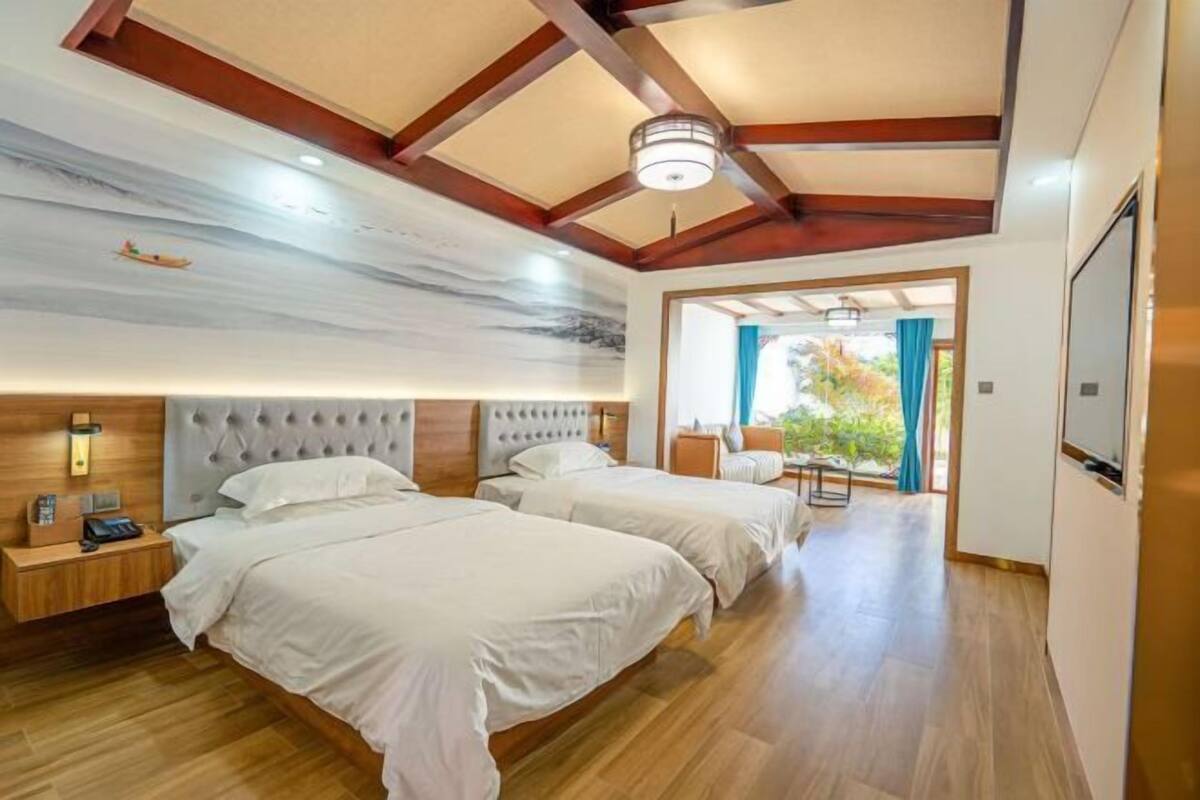 A hotel room with two beds, wooden flooring, a ceiling with exposed beams, and a view of the outdoors through a door.