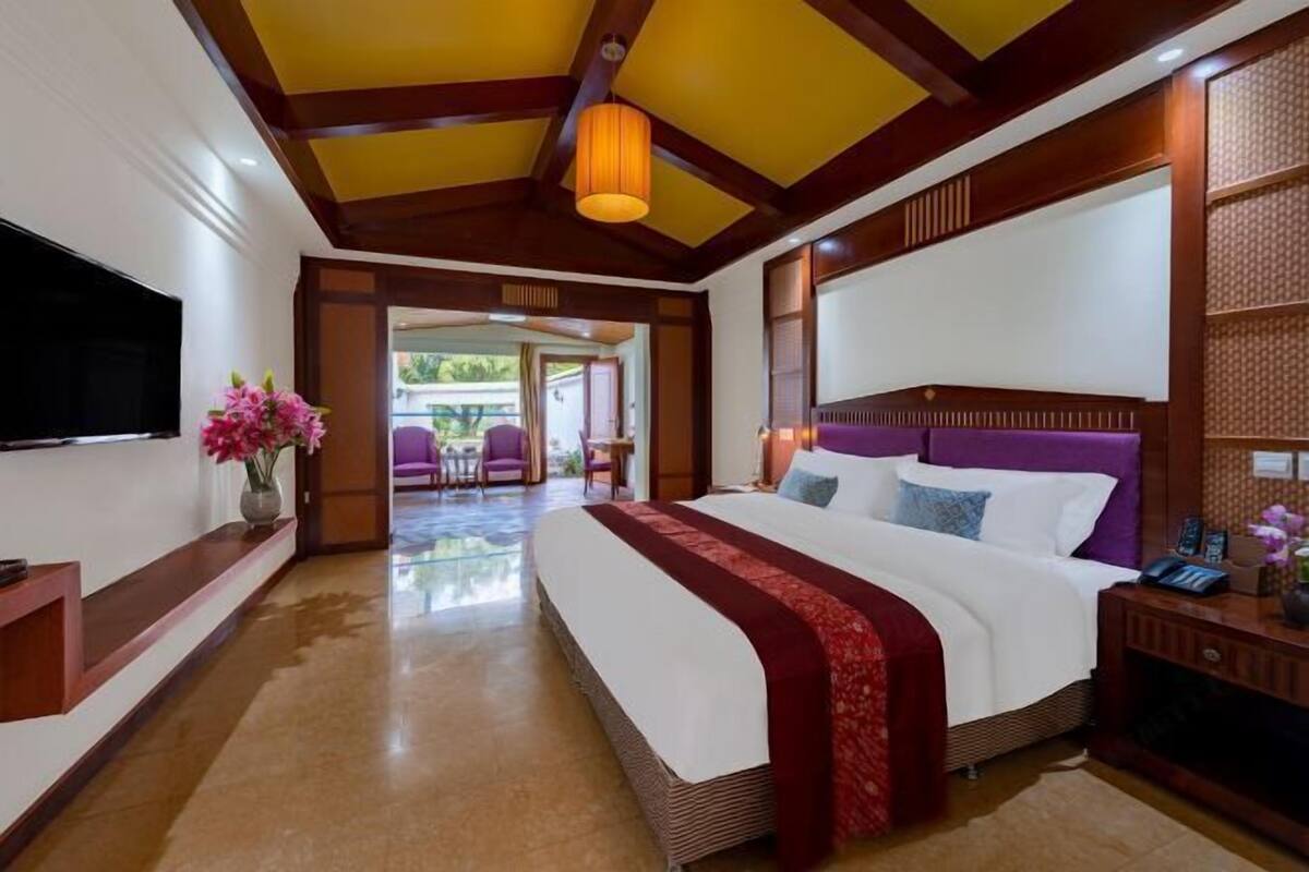 A spacious bedroom with a large bed, a TV, and a wooden headboard.