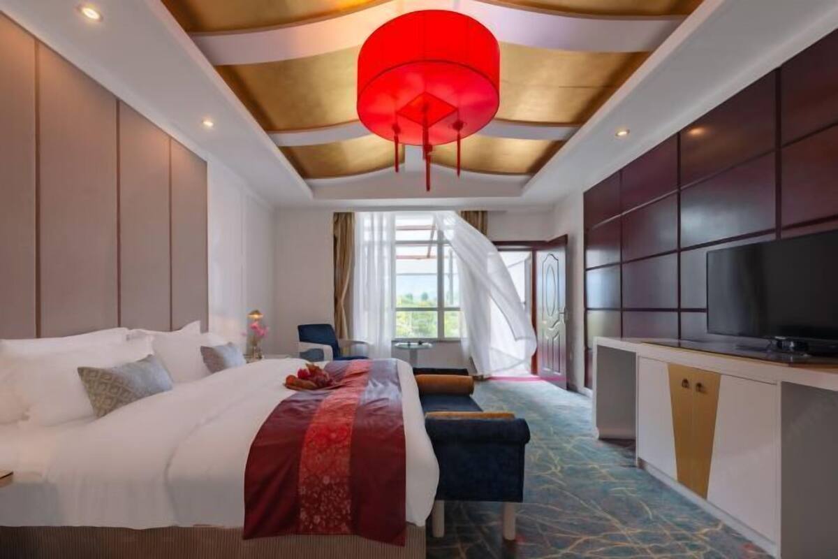 A hotel room with a large bed, a TV, a desk, and a view of greenery outside.