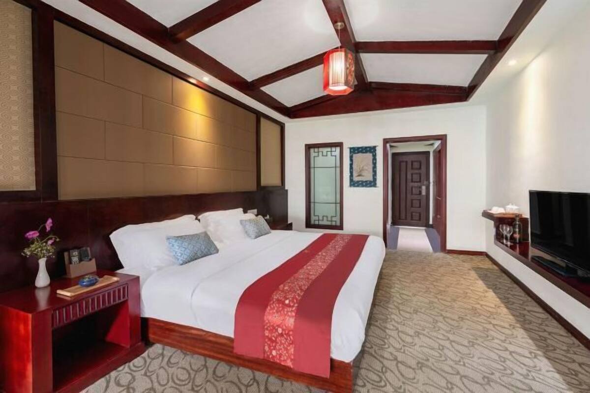 A hotel room with a large bed, wooden headboard, a TV, and a red decorative pillow.