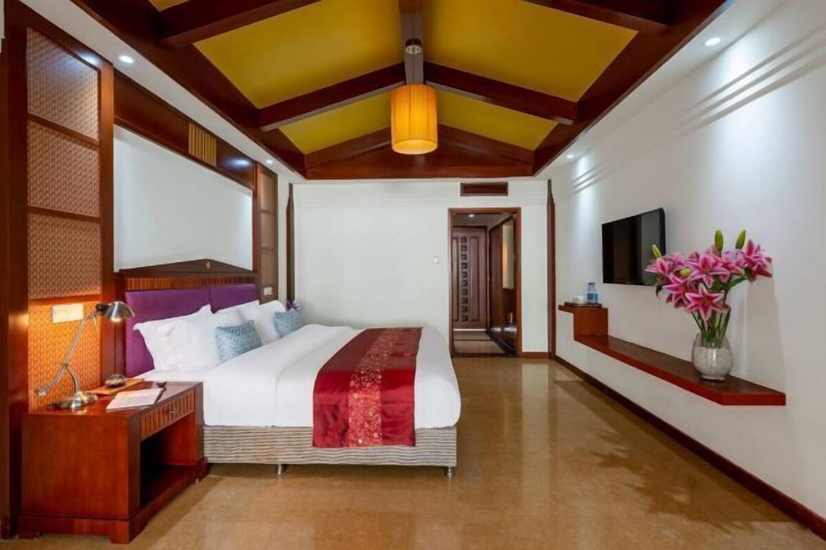 A hotel room with a large bed, a nightstand, a lamp, a TV, and a vase with flowers.