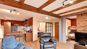 Amplia sala de estar con un sillón reclinable de cuero, un televisor y una cocina al fondo.